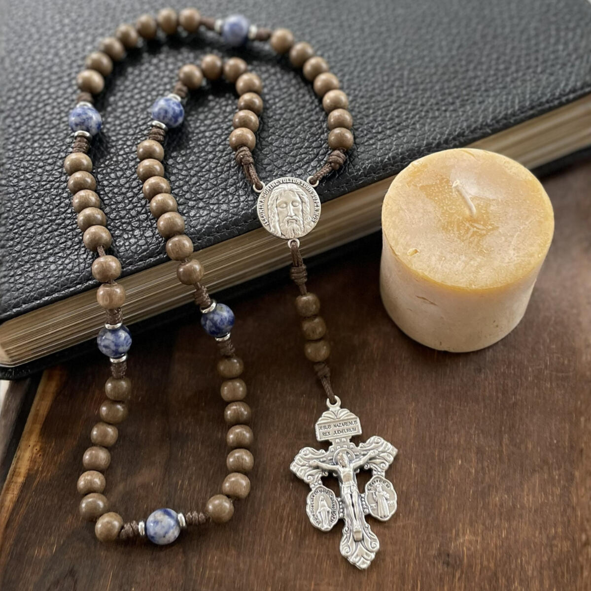 A handmade Seven Sorrows Rosary made from paracord with a silver Pardon Crucifix and silver Holy Face of Jesus centerpiece and the Hail Mary beads are grey brown wood and the Our Father beads are blue stone.