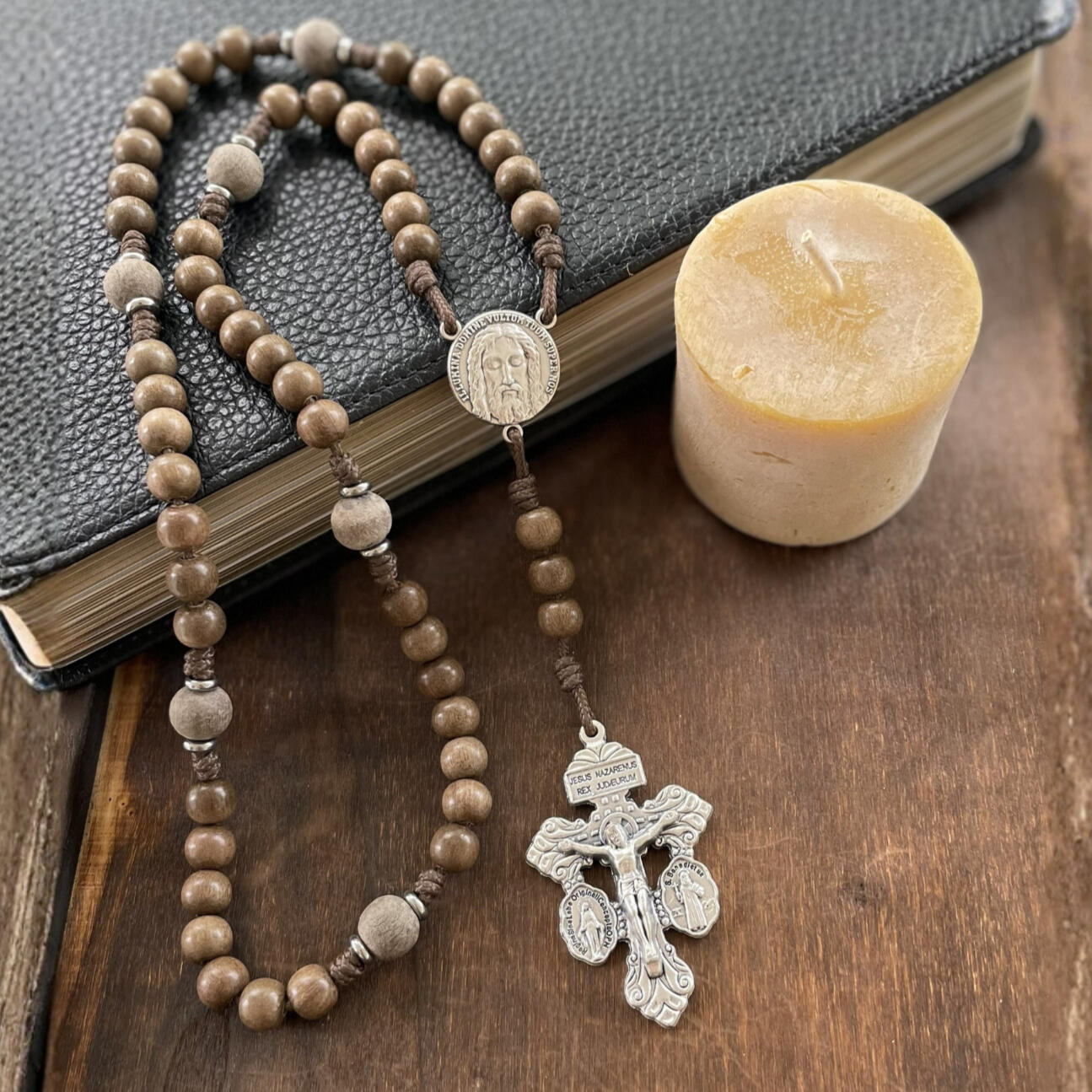 A handmade Seven Sorrows Rosary made from paracord with a silver Pardon Crucifix and silver Holy Face of Jesus centerpiece and the Hail Mary beads are grey brown wood and the Our Father beads are unfinished grey wood.