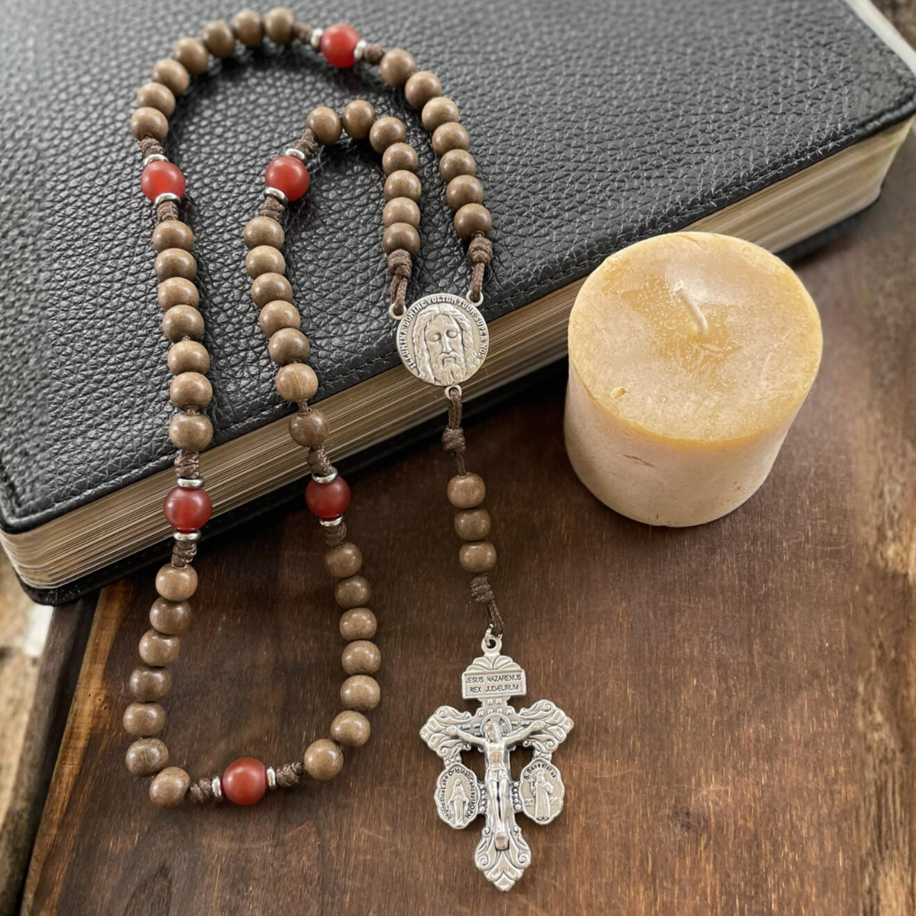A handmade Seven Sorrows Rosary made from paracord with a silver Pardon Crucifix and silver Holy Face of Jesus centerpiece and the Hail Mary beads are grey brown wood and the Our Father beads are red stone.