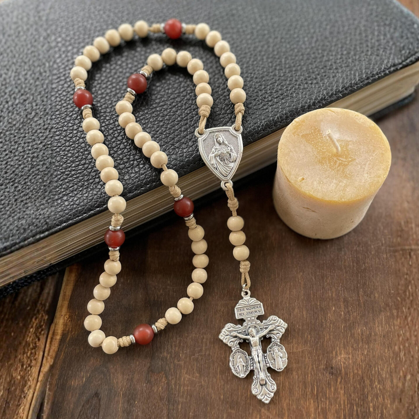 A handmade Seven Sorrows Rosary made from paracord with a silver Pardon Crucifix and silver Immaculate Heart of Mary centerpiece and the Hail Mary beads are cream color wood and the Our Father beads are red stone.